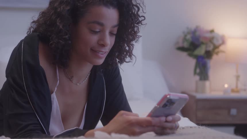 Woman smiling in bed while using smartphone