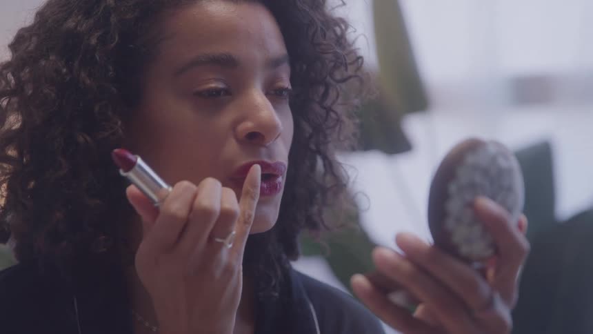 Woman applying red lipstick while looking into a handheld mirror