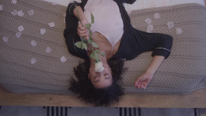 Woman lying on the bed with scattered petals holding a white rose