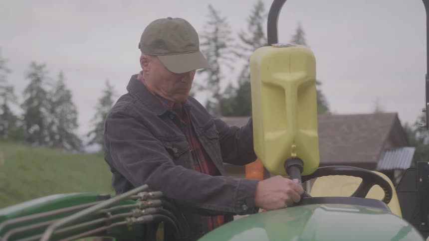 A middle aged man refuels an agricultural vehicle with a gallon outdoors during daytime