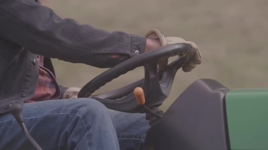 Man wearing gloves driving a tractor on a farm during the day