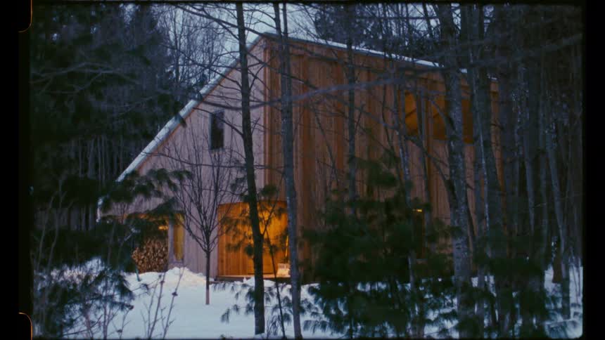 Wooden cabin lit up in the snow surrounded by trees