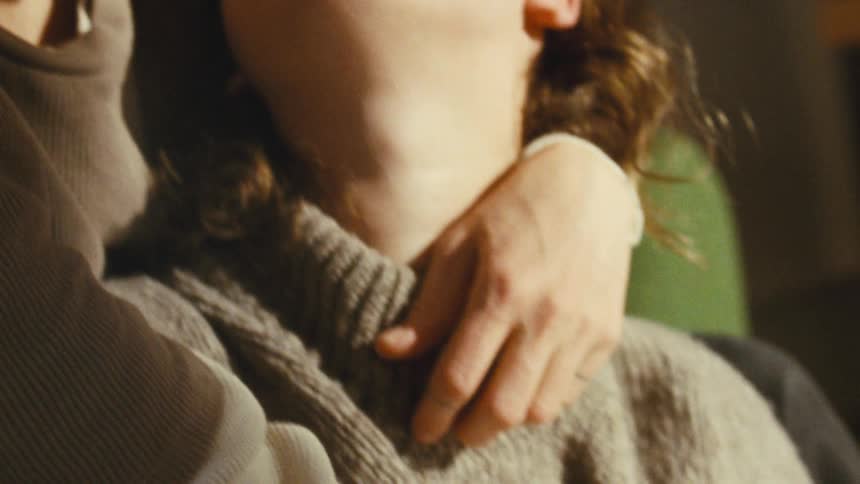 Close up of a young couple kissing and hugging each other while sitting in a living room during daytime