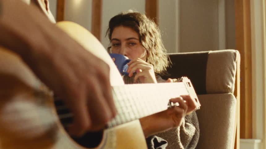 Woman drinking coffee while watching someone play guitar