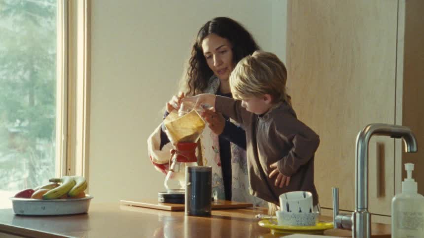 A woman and a young child are in a modernstyle kitchen preparing something on the island counter the woman helps the child pour liquid from a beaker into a pourover coffee carafe