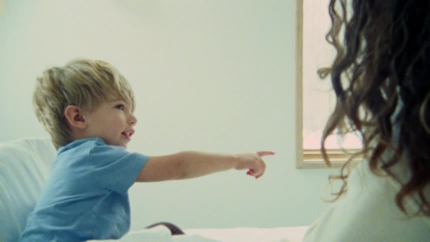 A toddler sitting in bed pointing something out to his mother