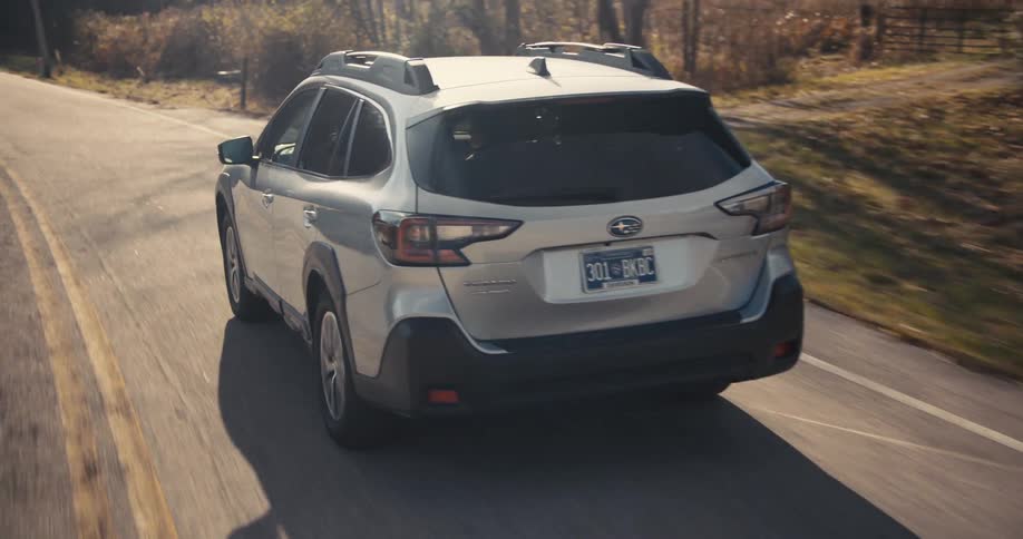A silver subaru outback travels along a remote road lined with trees