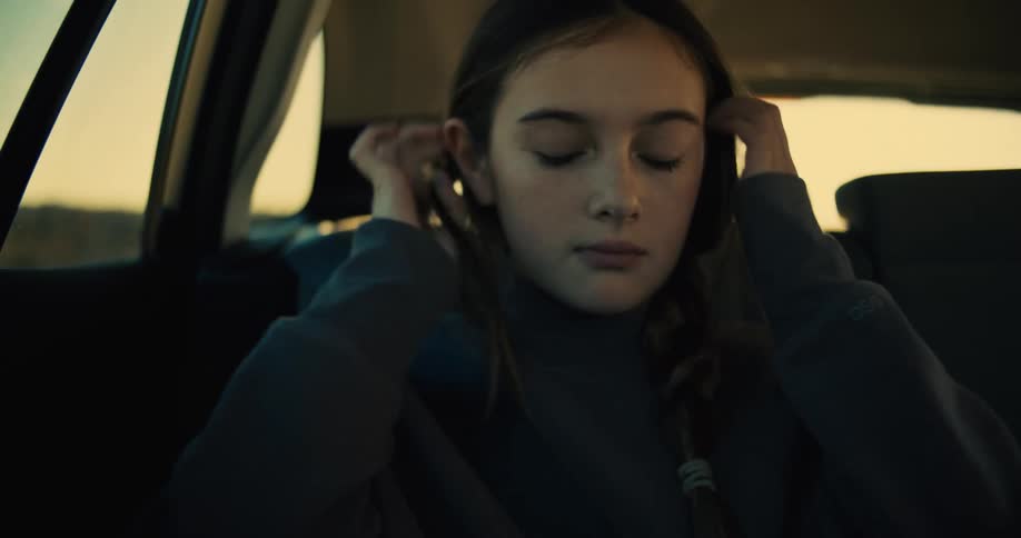 Girl sitting in the back seat of a car looks down