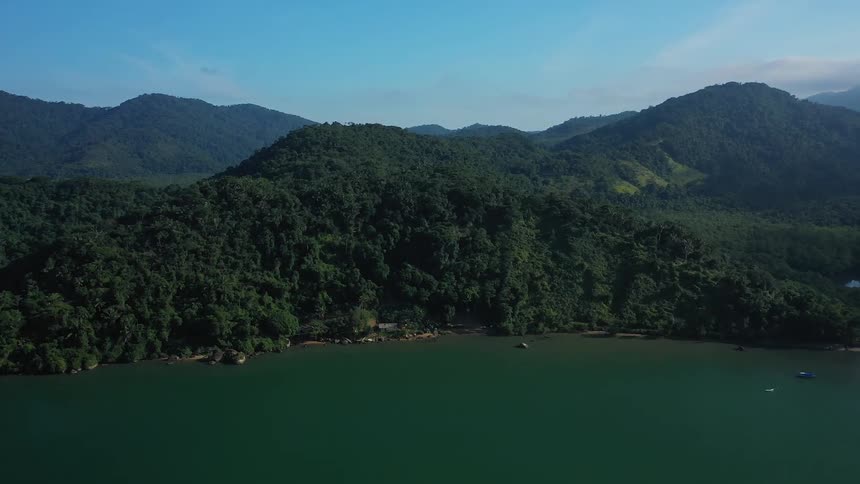 A lush green forested mountain range beside a calm body of water
