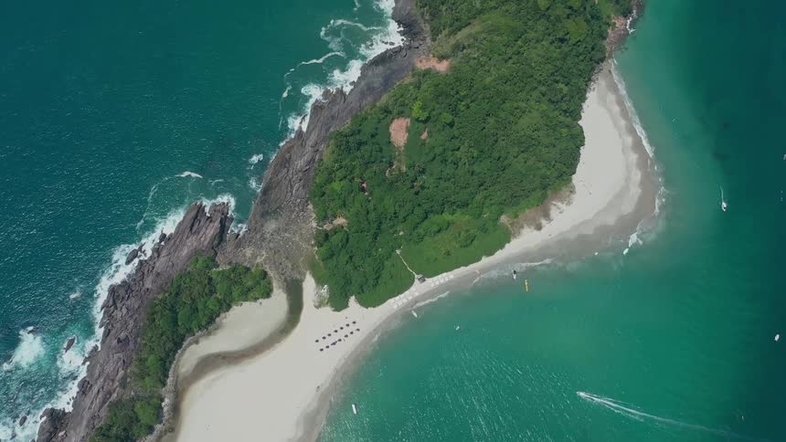 An aerial view shows a stunning bay with rocky outcrops and a sandy beach the turquoise water is crystal clear revealing the seabed below a few small boats are anchored in the calm water near the shore