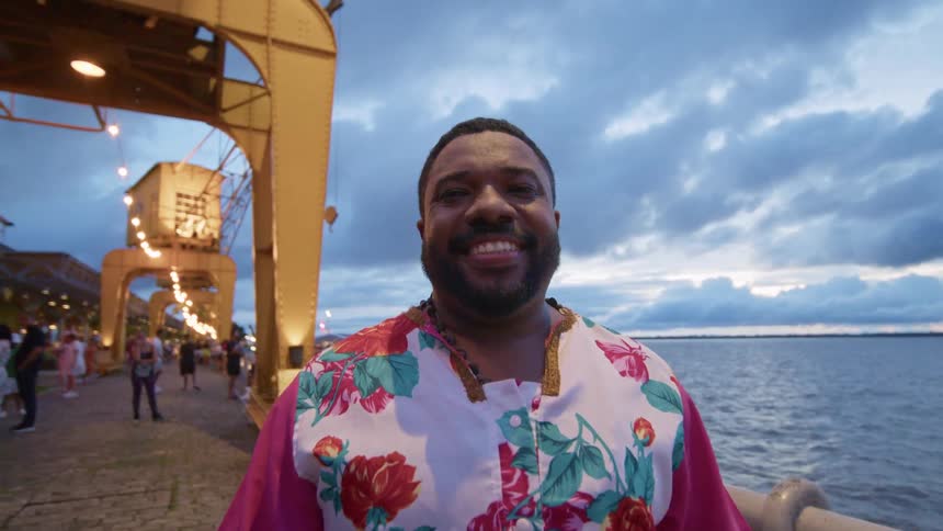 A man stands on the beach near the boardwalk and smiles