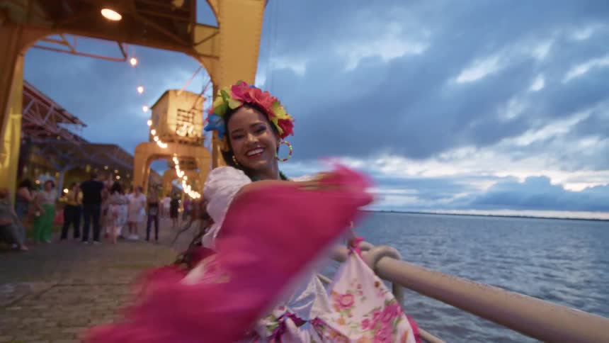 Smiling dancer in traditional colorful attire performing by the riverside