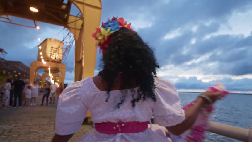 A woman in a colorful dress is dancing by the water