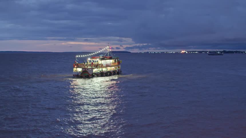A brightly lit ferry is transporting people to the shore