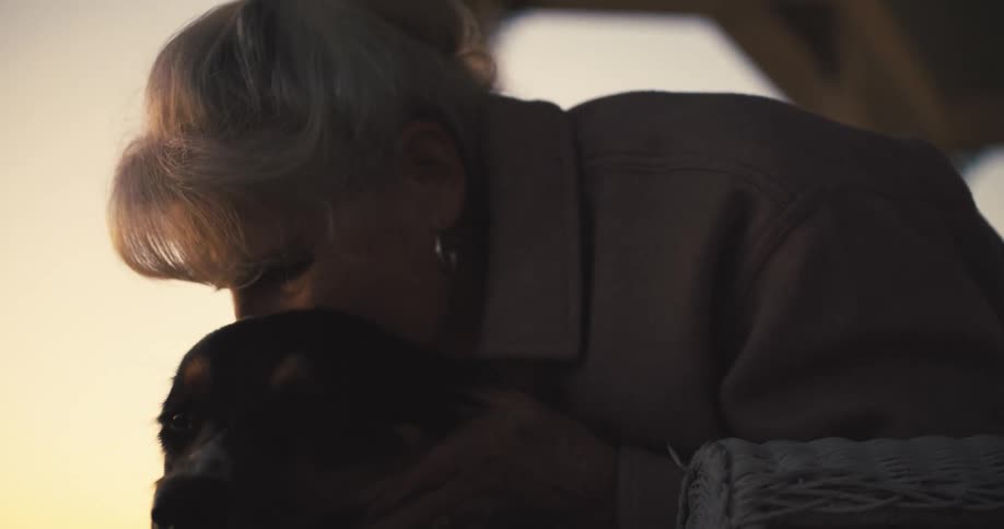 Elderly woman gently cuddling her dog at sunset
