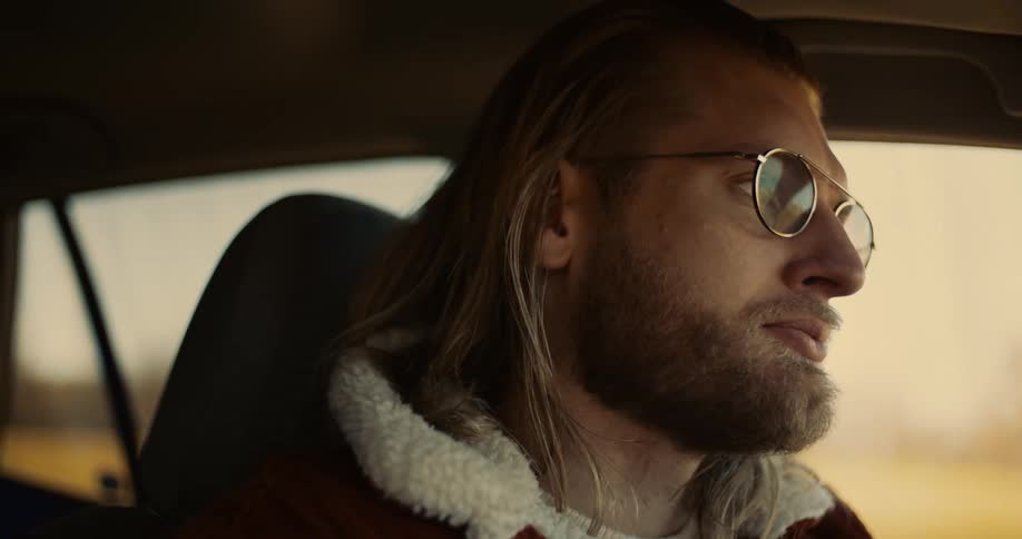 Man with glasses and a shearling jacket driving a car
