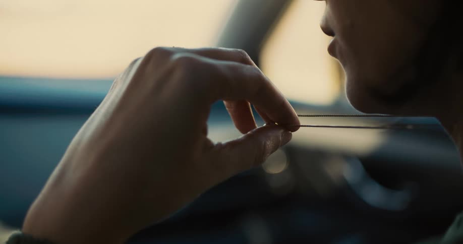 Woman sitting inside her car comtemplating while fidgeting with her necklace