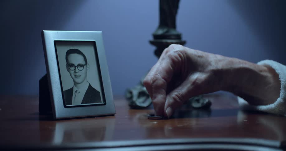 Elderly woman placing her wedding ring on nightstand next to husbands photo