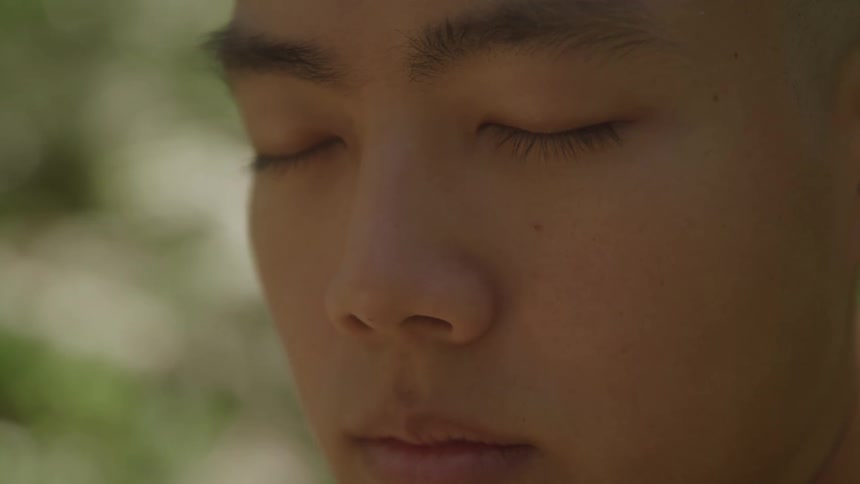 An asian mans face with his eyes closed outside likely meditating
