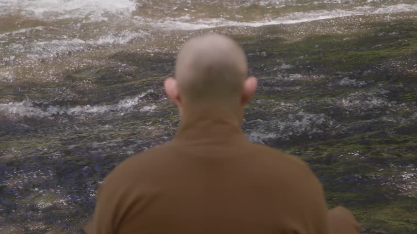 A bald man watches a river