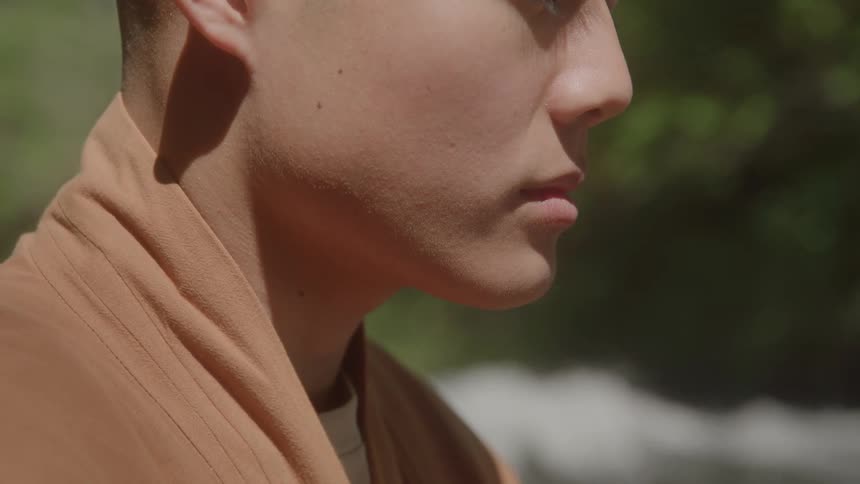 A person in a brown robe is shown in profile eyes closed with a blurred natural background