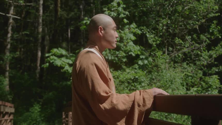 Monk standing with calm expression in forest