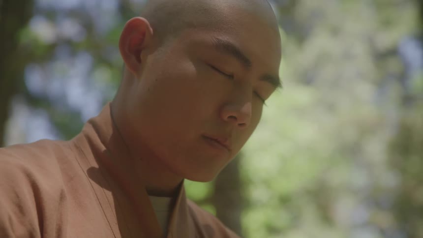 Person with closed eyes wearing traditional brown attire in a natural setting