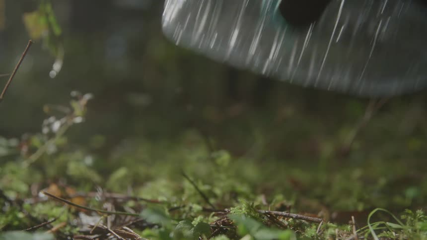 A grabber tool is used to pick up a discarded plastic bottle cleaning up litter from the mossy ground in a forest