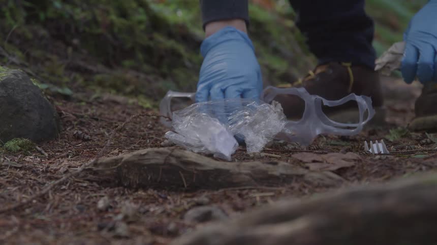 Close up of a hiker in brown boots cleaning up discarded trash on a trail