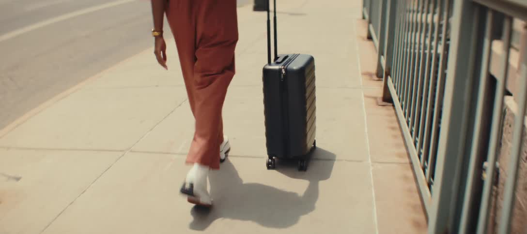 Woman pulls her luggage as she walks on a downtown sidewalk