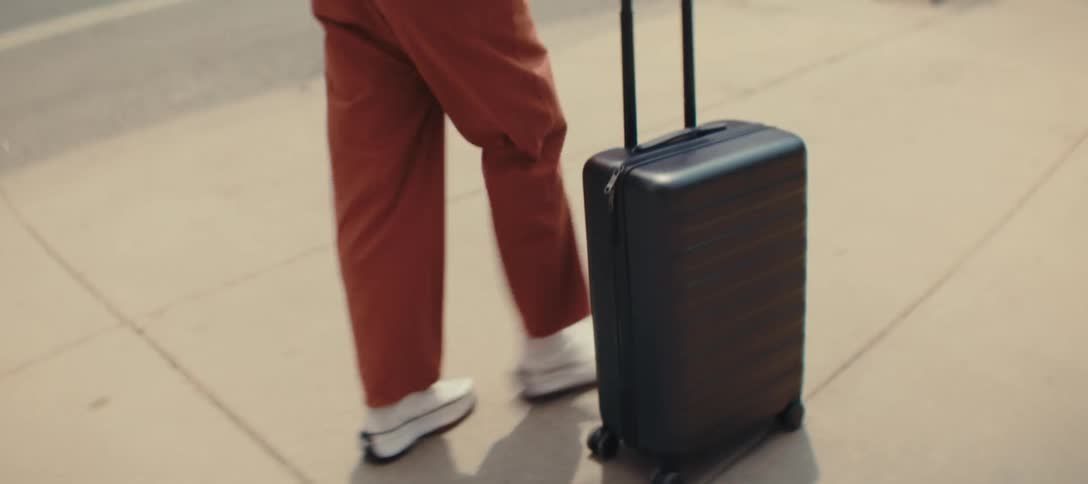 Person pulling a black wheeled suitcase on an urban sidewalk