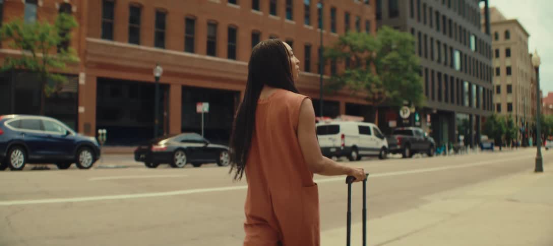 Woman pulls her luggage as she walks on a downtown sidewalk looking around