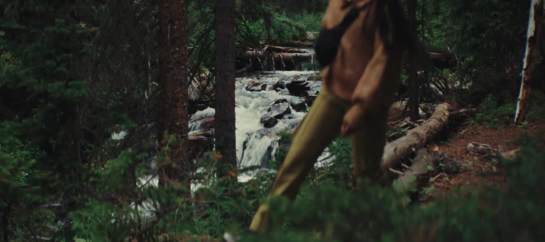 Person walking in a forest near a stream with small waterfalls