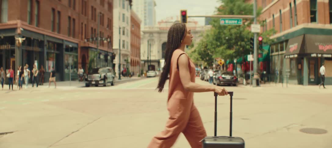 A woman crossing a city street while pushing a luggage trolley bag beside her