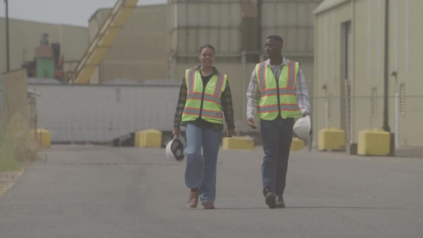 Two workers in reflective vests walking through the industrial yard