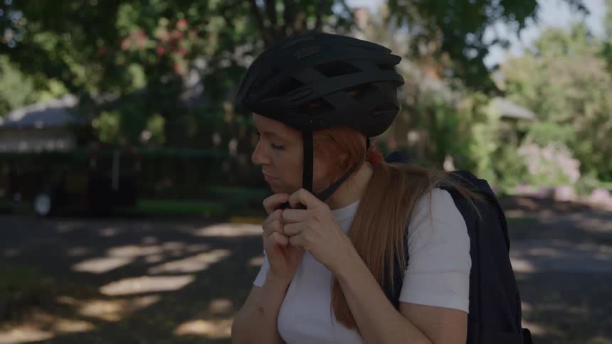 Woman adjusts her cycling helmet on a treelined street