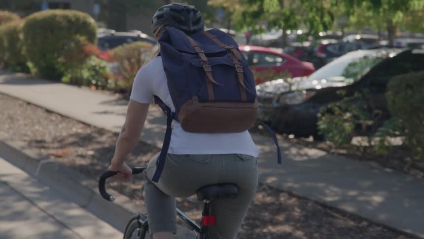 Cyclist with a blue backpack rides along a treelined street