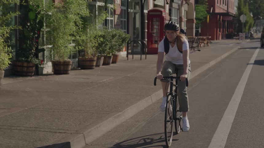 A young woman rides a bicycle down a city street in daylight
