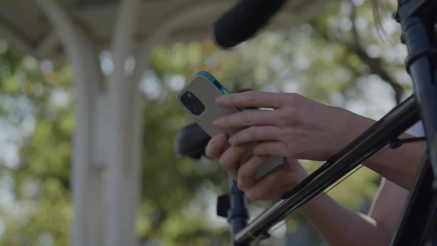 Hands holding a smartphone near a microphone setup outdoors