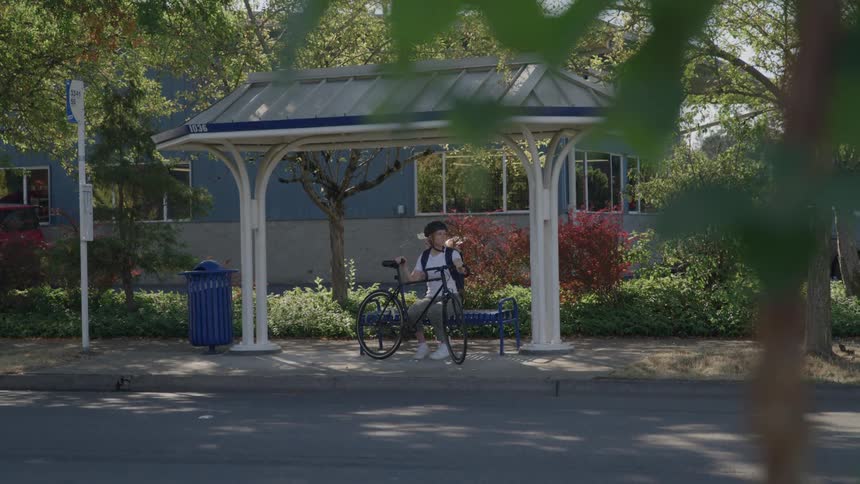A girl sitting at a bus stop holding her bicycle and waiting for something or someone