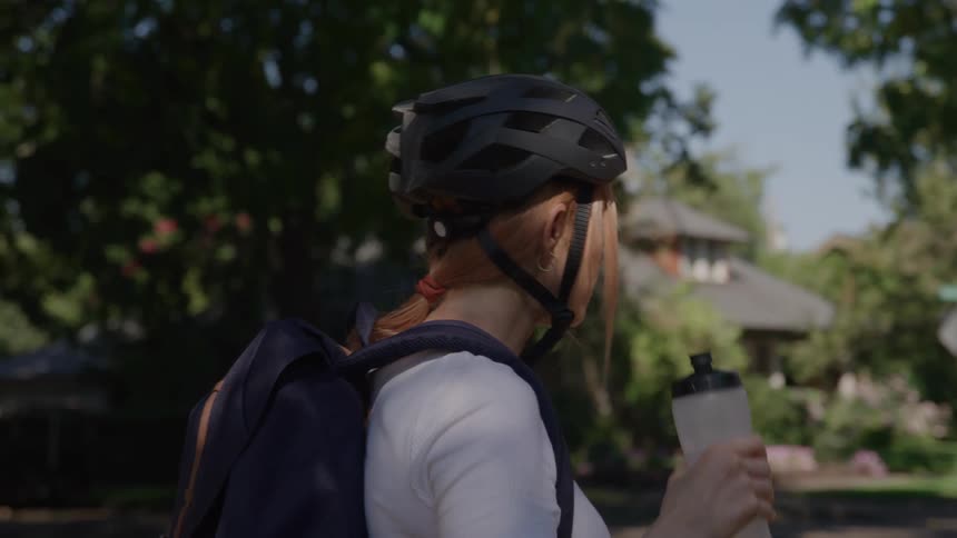 Woman wearing bike helmet drinks water outside