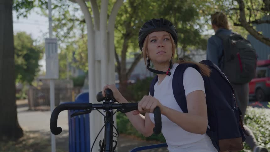 Cyclist with helmet and backpack holds the bicycle at a bus stop