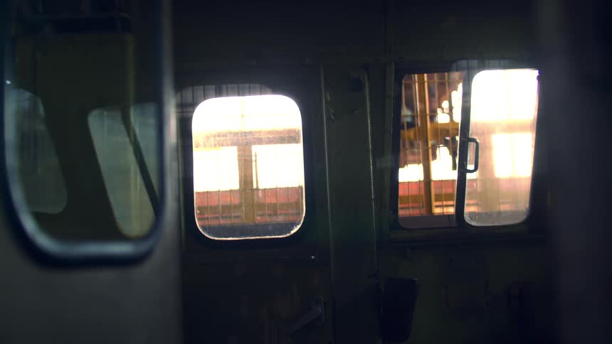 A dark interior of what appears to be a train engine is shown from a forward facing view with light colored windows on the right and front that illuminate a control panel and a handle