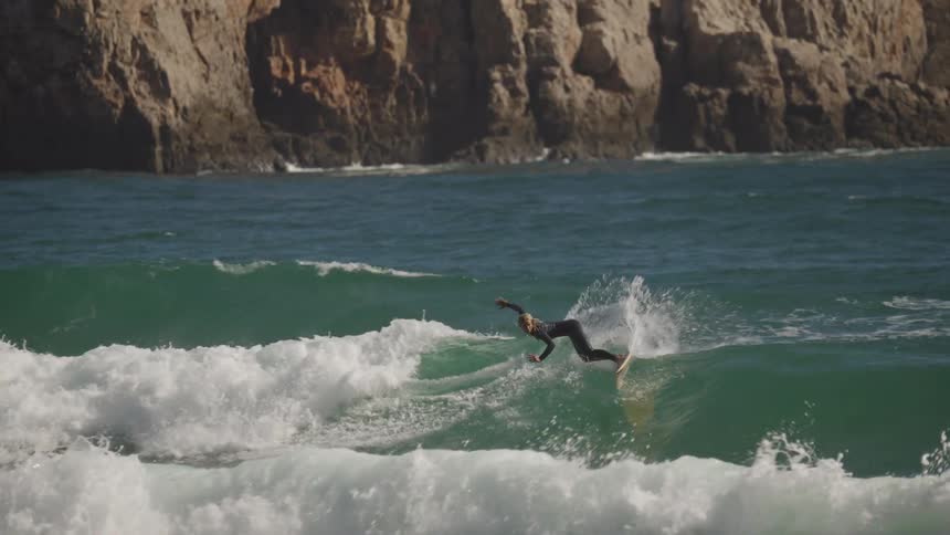 Several men are on surfboards catching waves at a mountainous beach