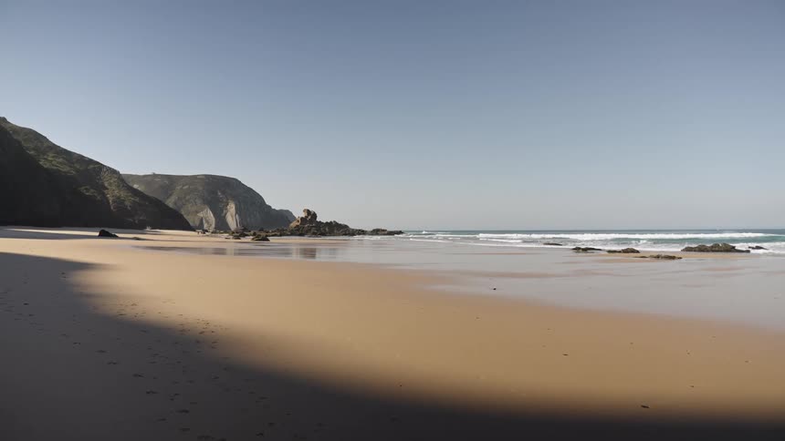 A serene empty beach with rocky cliffs under a clear blue sky