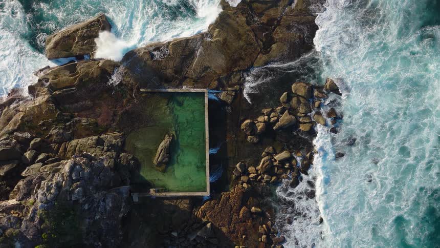 Overhead view of a rectangular ocean pool amid waves and rocky shore