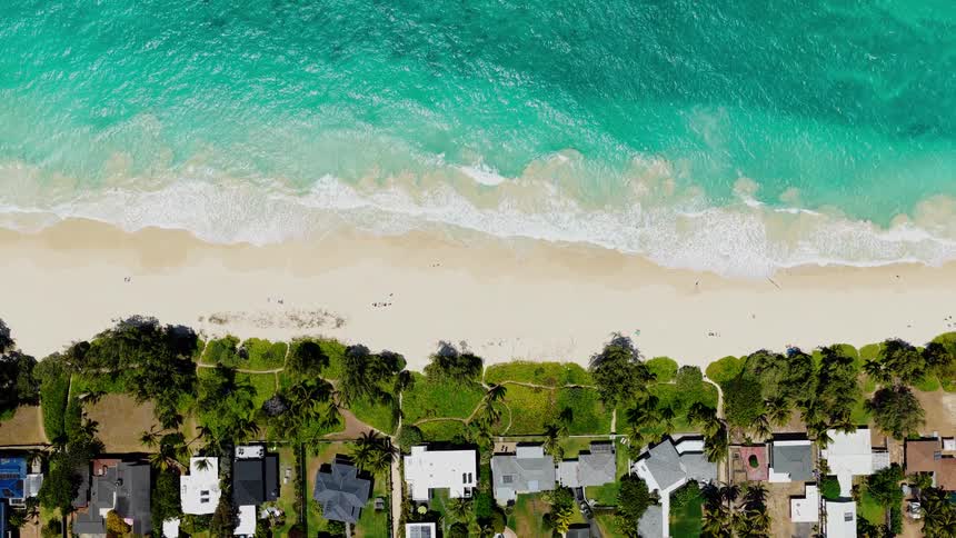 Aquamarine surf flows onto the beach near a residential neighborhood