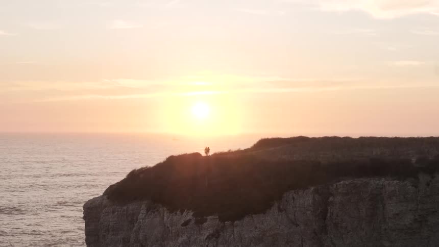 Two people stand by the cliff of the ocean
