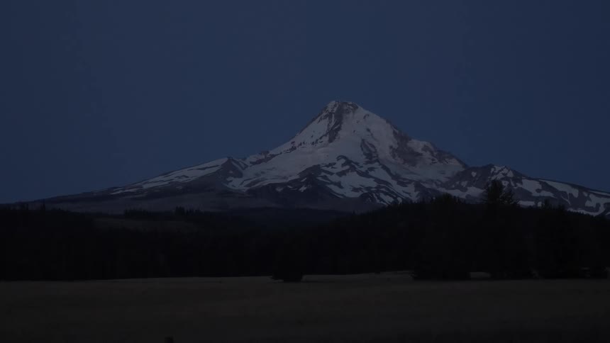 A snow covered mountain peak rises under a dusky sky