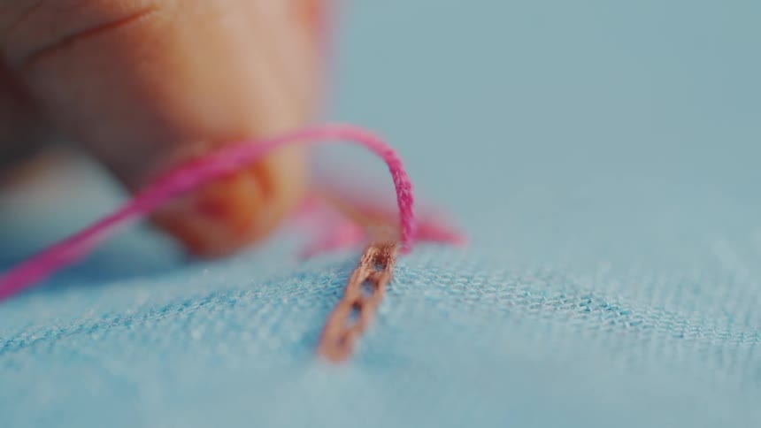 Hand sewing blue fabric with pink and brown thread